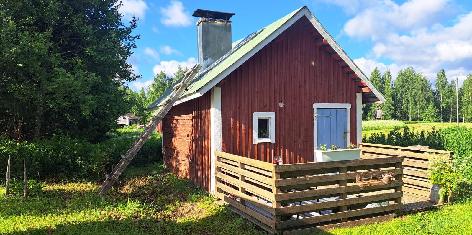 Punainen vanha sauna kesäisessä maisemasssa.